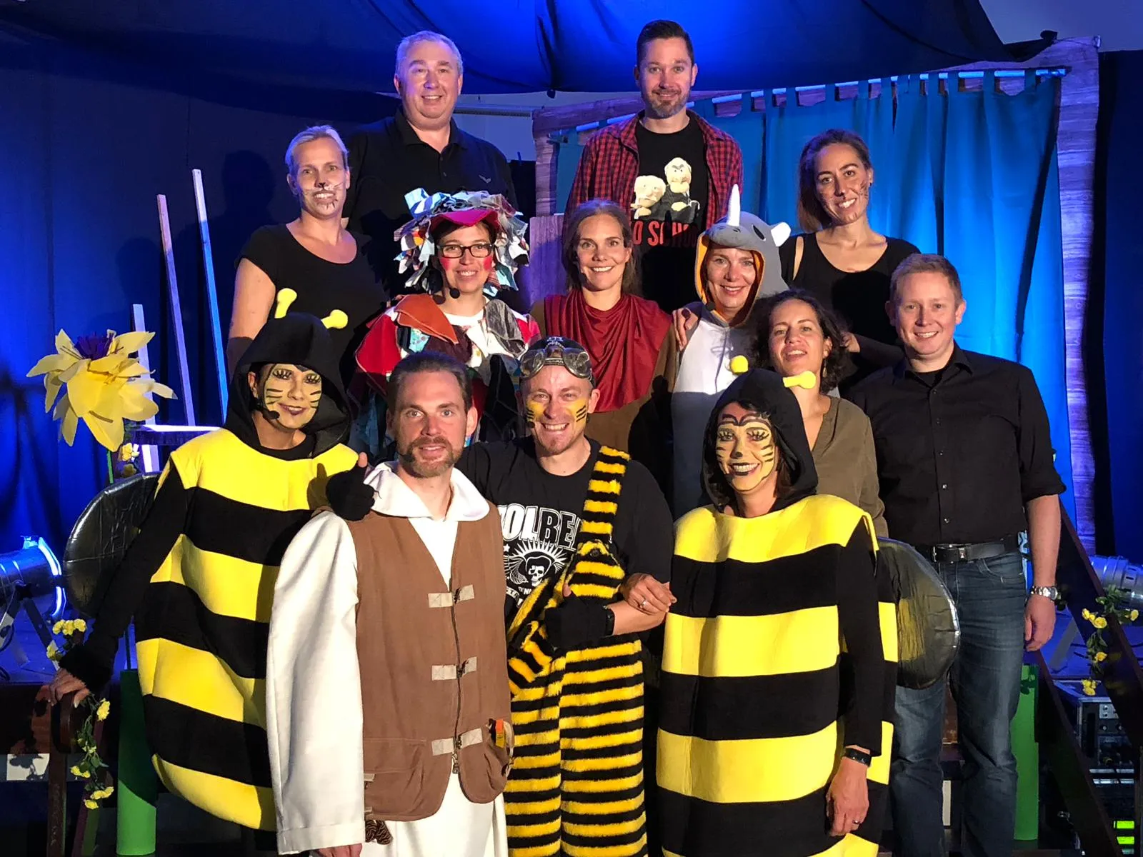 Gruppenfoto des Ensembles von „Arche Noah“ in Kostüm — Bienen, Einhorn, Katzen und weitere Tierfiguren vor blauer Kulisse.