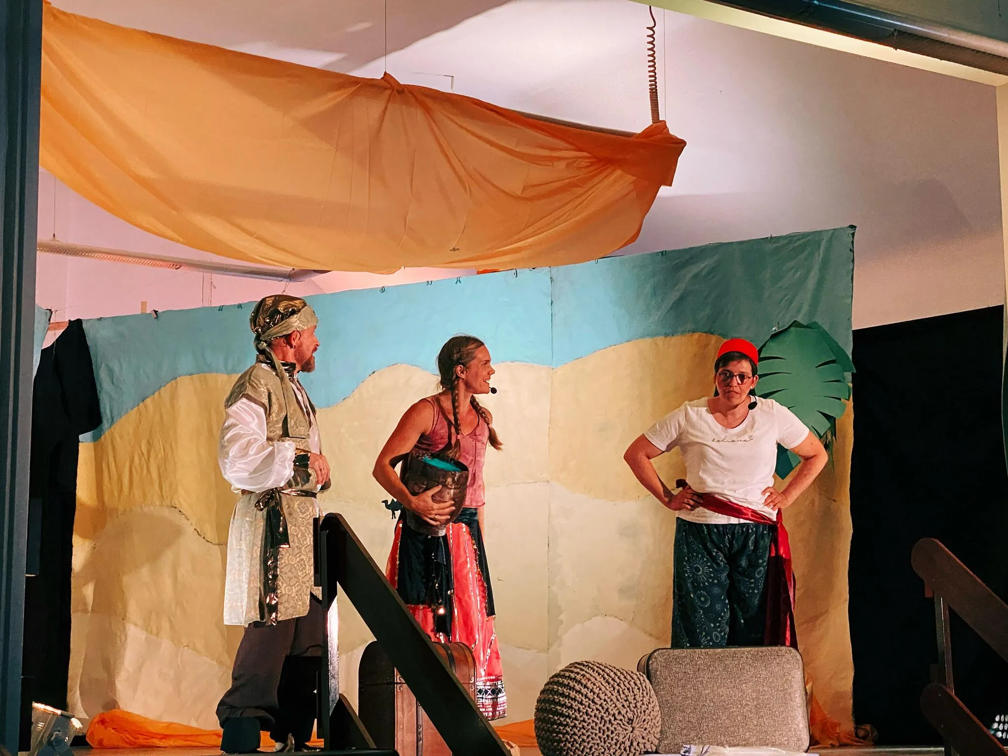 Sultan, eine Verkäuferin mit Krug und eine Figur mit rotem Fes im Gespräch.