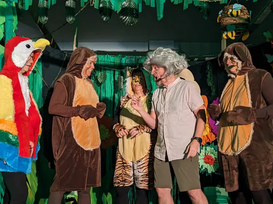 Papagei, zwei Affen, eine Tigerfigur und der ängstliche Forscher Fritz mit grauer Perücke im Gespräch vor der Dschungelkulisse.